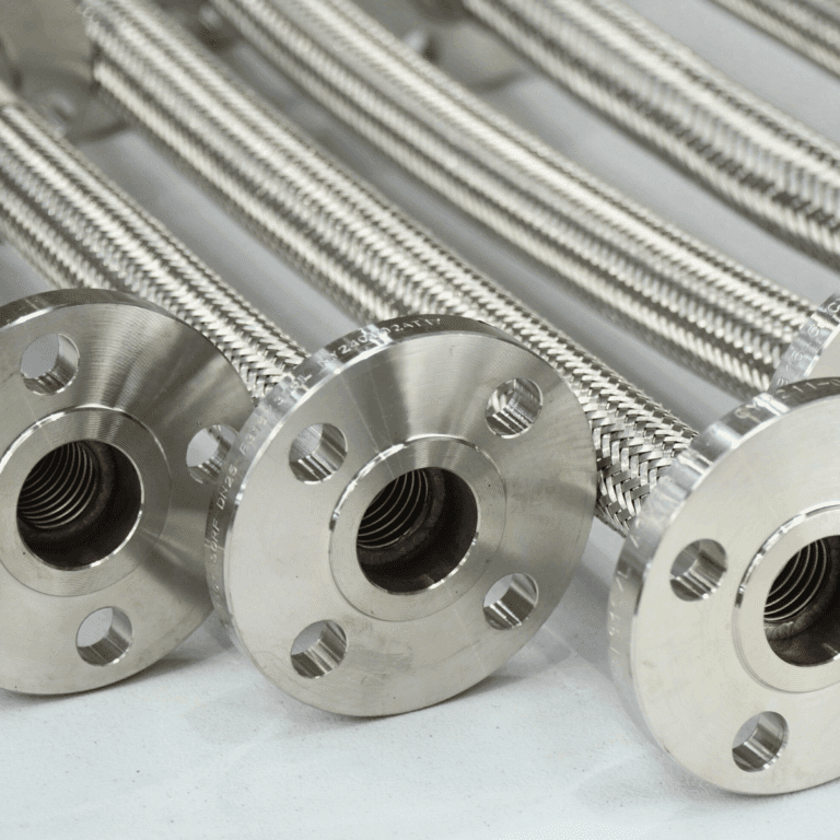 Close-up of several flexible metal braided hoses with circular flanged ends, arranged in parallel on a light surface, showcasing their polished, industrial appearance.